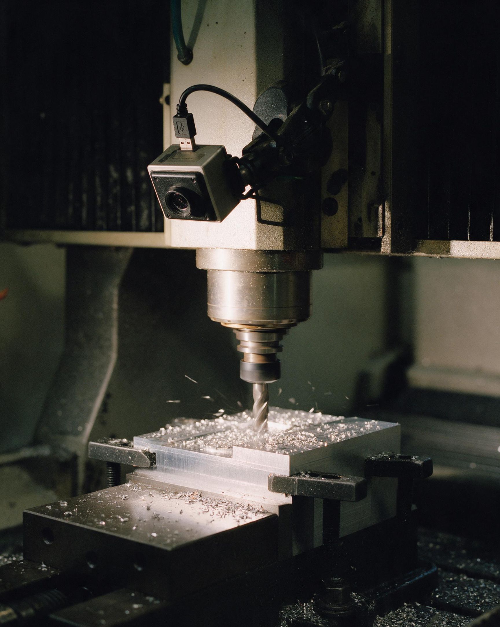 A small camera clamped to a CNC gantry, watching the cut.