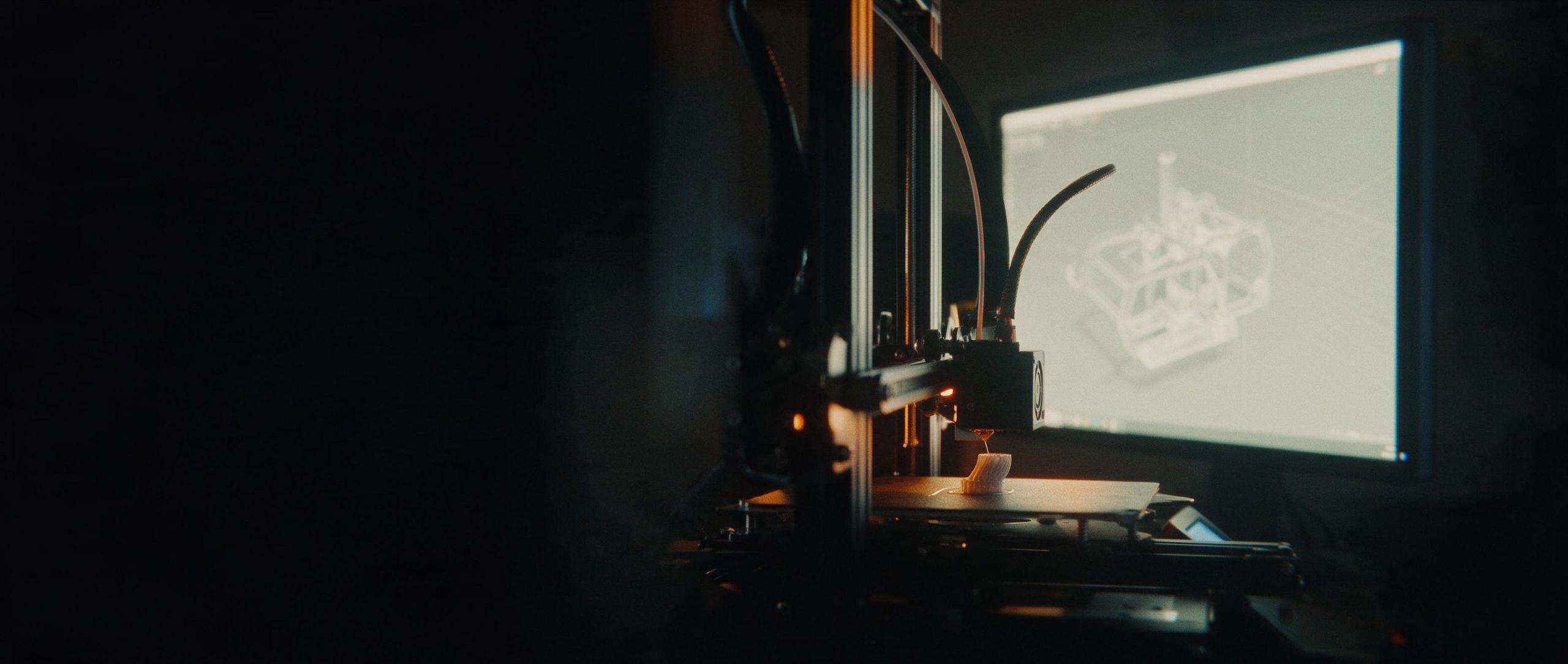 A 3D printer at work beside a monitor glowing with its digital twin.