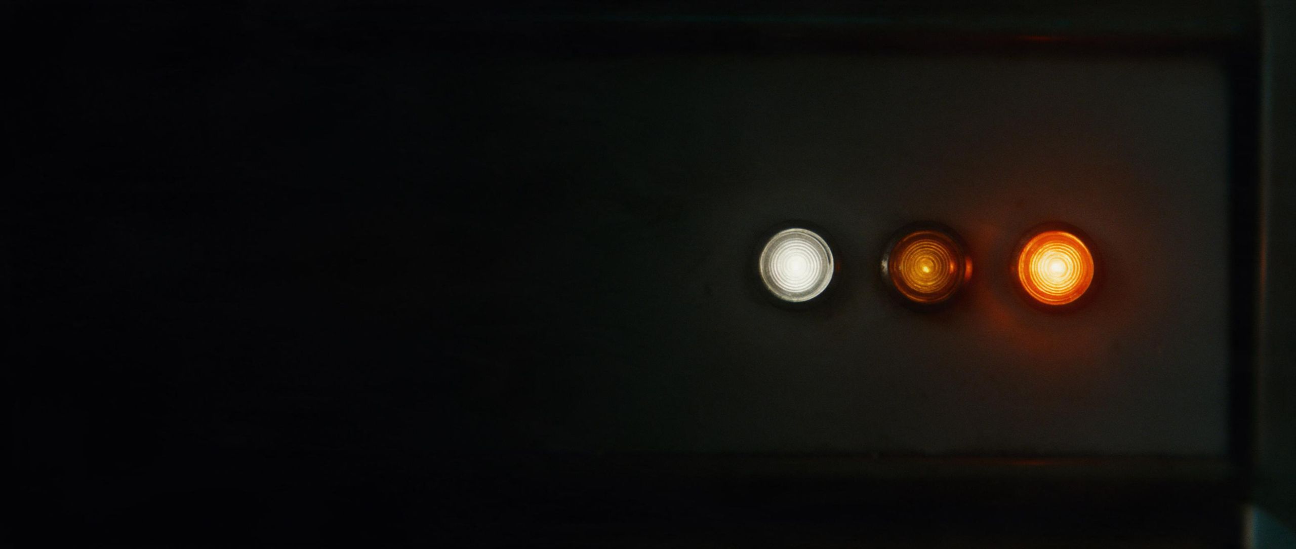 Tres pilotos en un panel oscuro; el último, encendido en naranja.