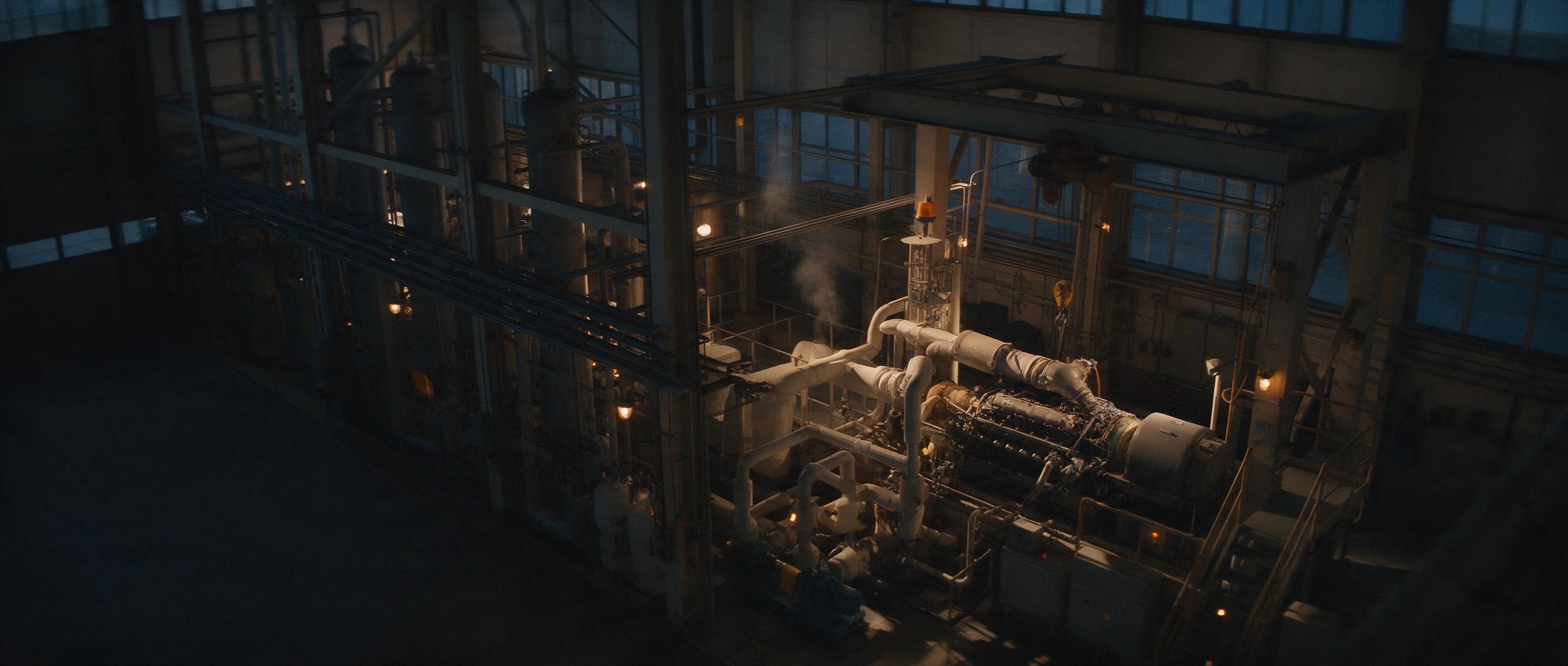 An industrial test hall at blue hour, pipework, tanks and a test stand running with no one on the floor.