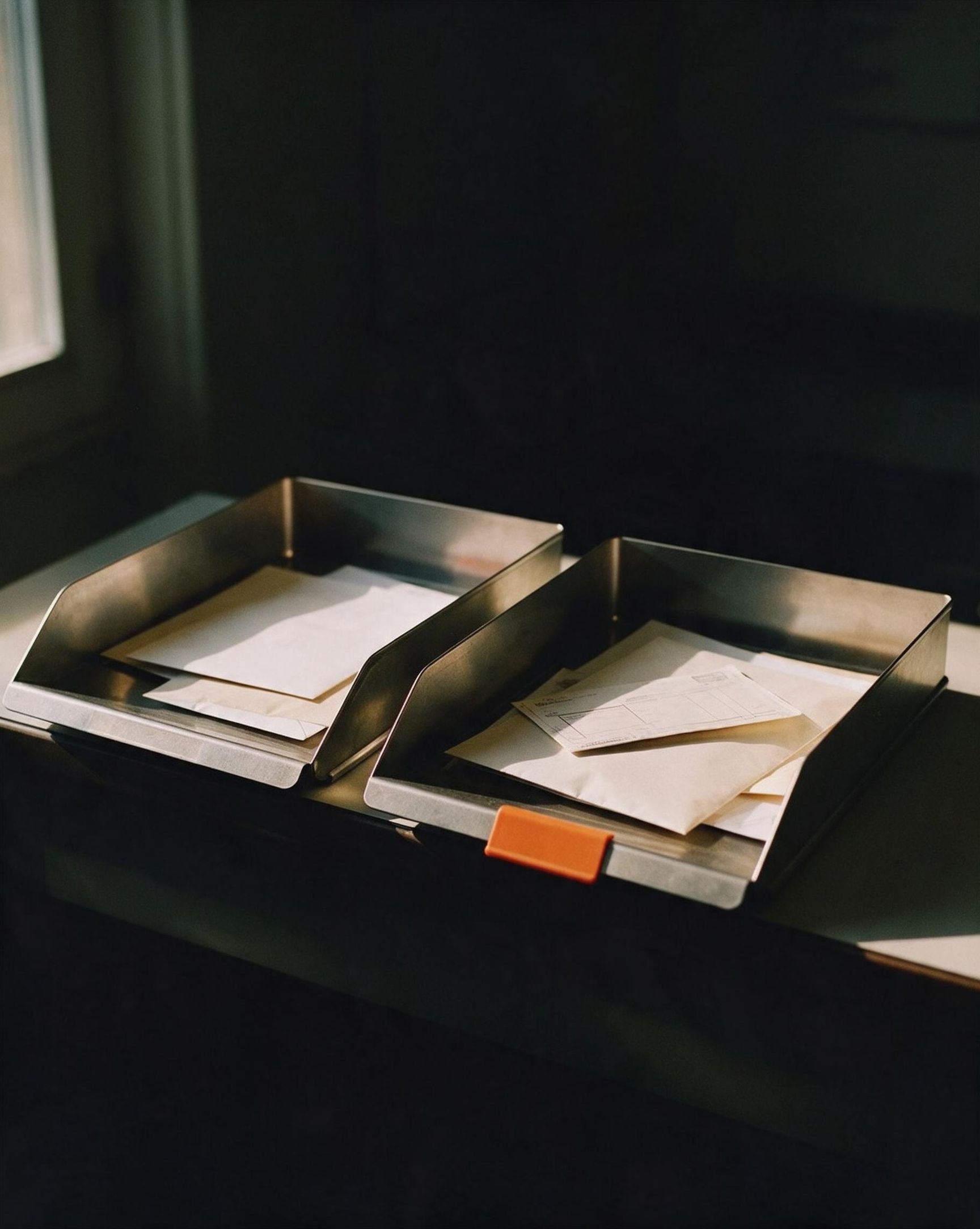 Two letter trays on a desk holding envelopes.