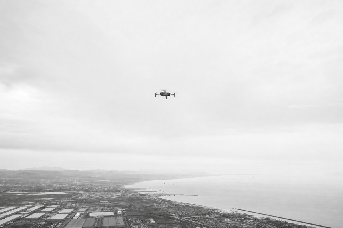 Un solo dron en vuelo sobre techos, un patio y una costa.